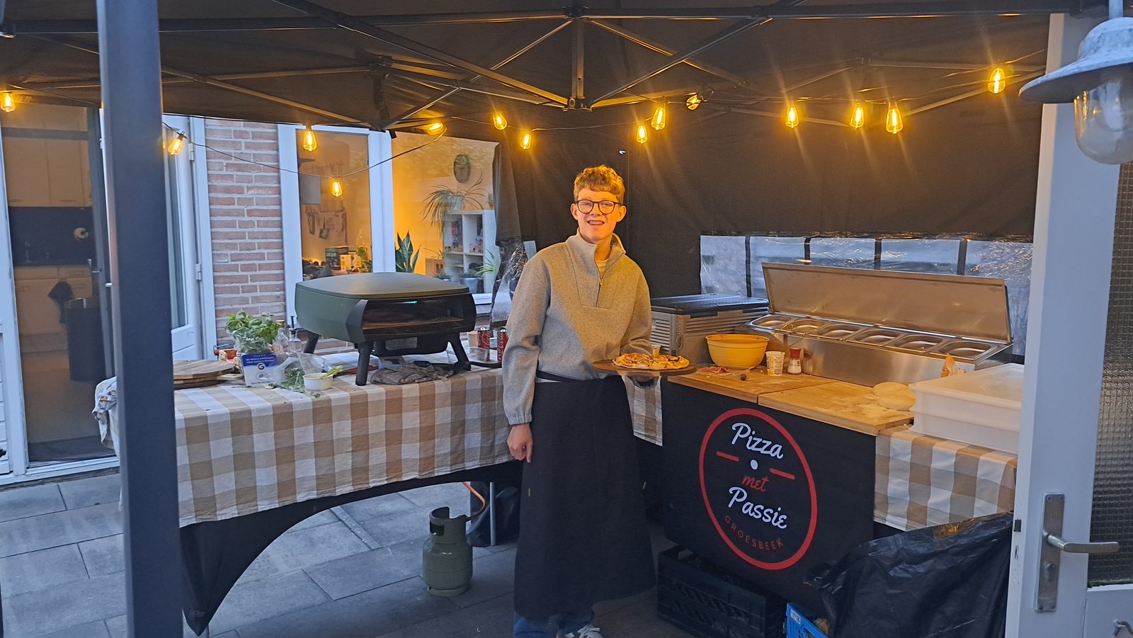 Pizzabakker van Pizza met Passie met een verse pizza bij de pizzakraam onder de lampjes